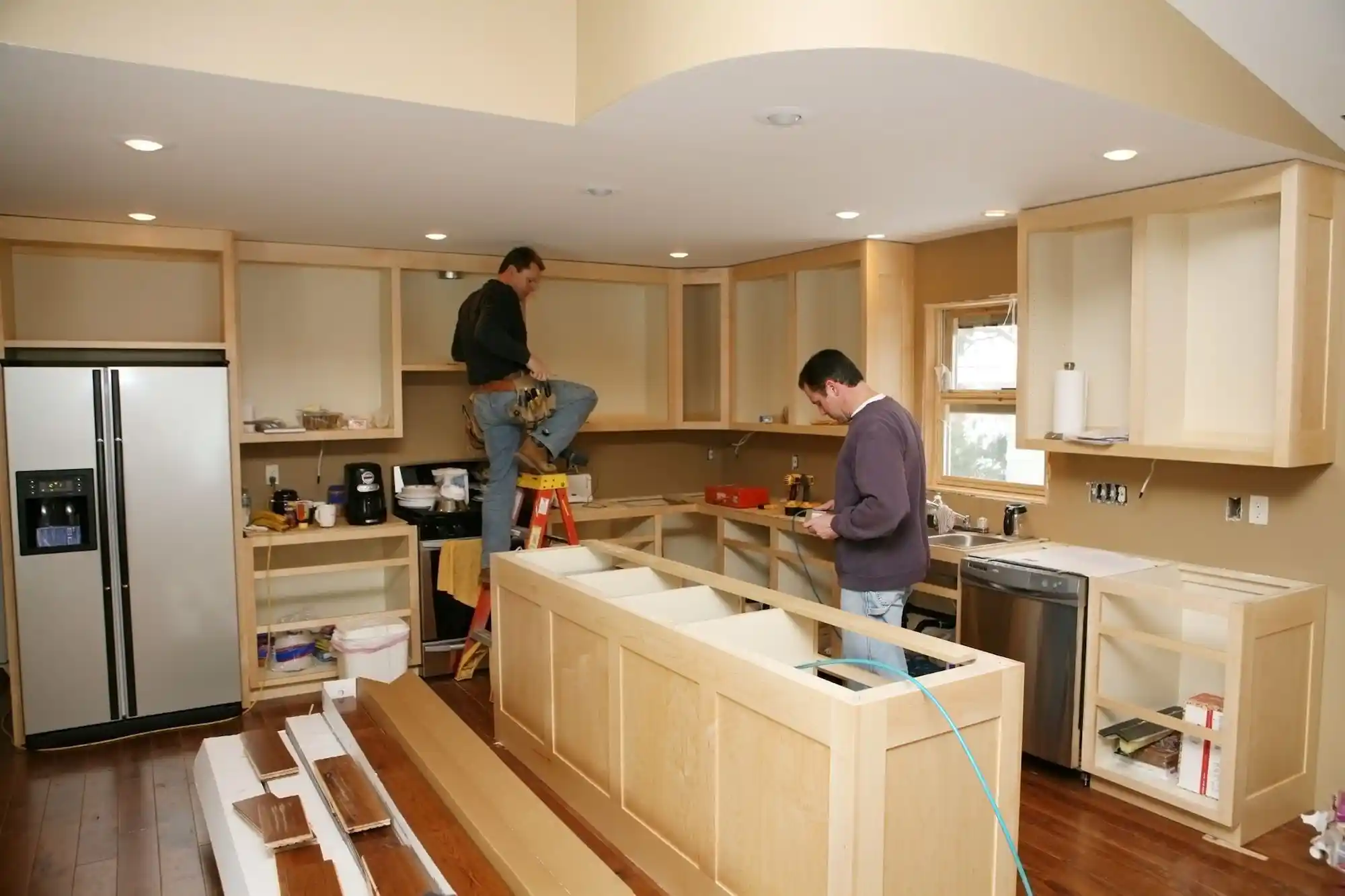 Installers confirming final measurements while fitting new kitchen cabinets and an island